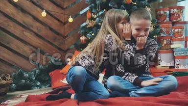 可爱的孩子们在彼此耳边低语秘密，坐在家里的<strong>红毯</strong>子上，庆祝圣诞节。